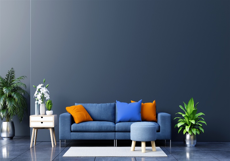 Imagem de uma sala de estar com paredes e sofá azuis, com almofadas na cor laranja