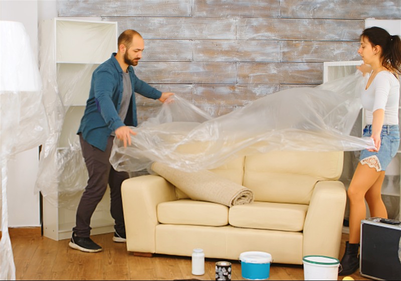 Imagem de um casal cobrindo um sofá para reformar a casa