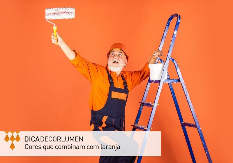 Imagem de um pintor em uma escada pintando uma parede de laranja