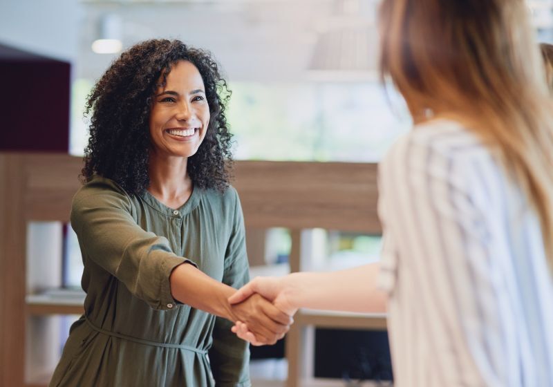 Mulher sorrindo e cumprimentando outra pessoa